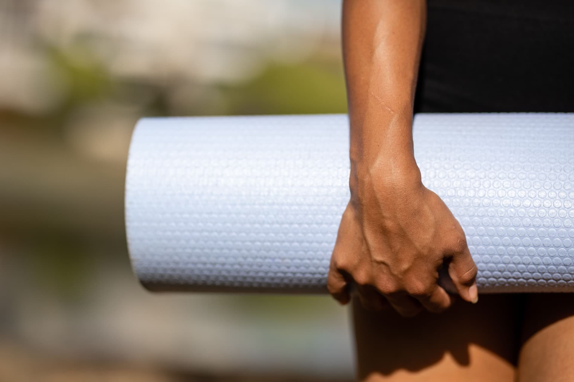 Una mano sosteniendo una esterilla de yoga enrollada, a contraluz